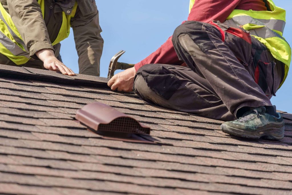 Professional roof installation: worker with safety equipment standing on newly shingled roof under daylight.